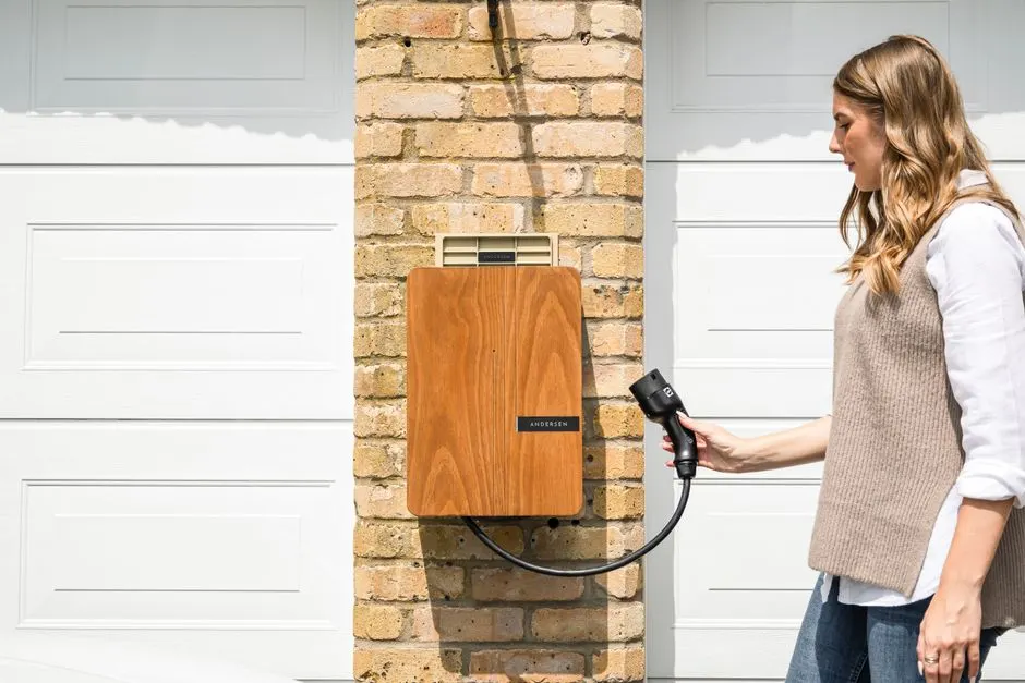 Une wallbox blanche fixée au mur d'un garage, câble branché sur une voiture électrique.